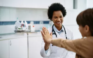 happy african american pediatrician gives high five to kid after medical examination at doctor's office.